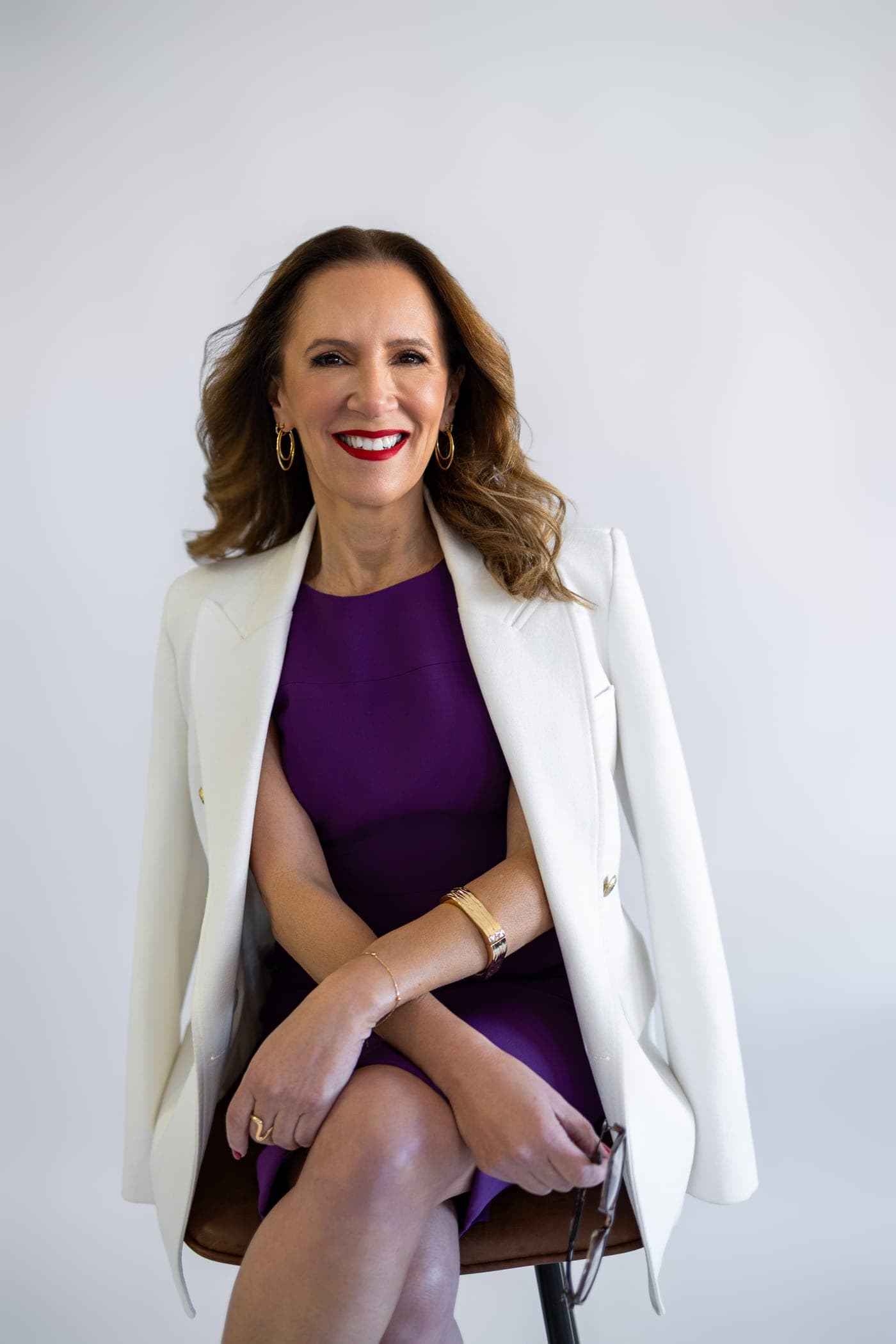 Gláucia Miranda Pires, de vestido roxo e blazer branco, sentada